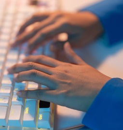 Hands typing at a white illuminated keyboard