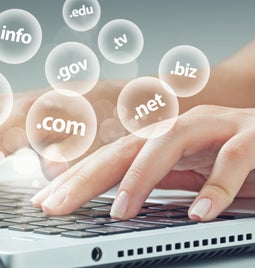 Woman's hands typing at a laptop with clear bubbles floating above showing different domain name extensions