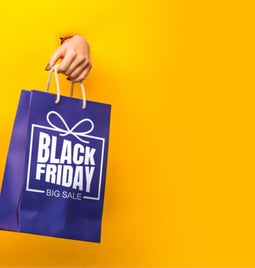 Hands popping out of a yellow backdrop holding Black Friday Cyber Monday branded shopping bags