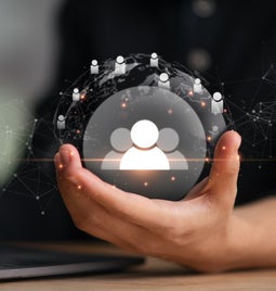 Hand holding visual art of the world, with people icons scattered over its surface and three large people icons in the middle of the sphere