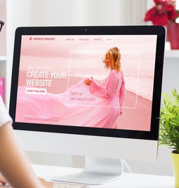 Woman sitting at desk looking at a desktop screen with a pink image of a woman on a beach