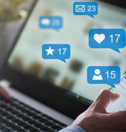 Hands typing on a laptop and holding a phone with social media interactions on screen