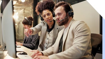 Two people looking at a computer screen with headsets on