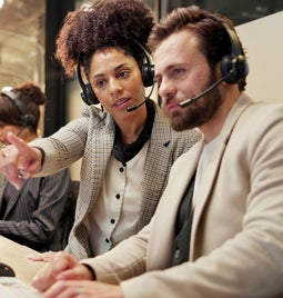 Two people looking at a computer screen with headsets on
