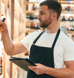 Male employee in an apron placing a bottle of alcohol on to a shelf