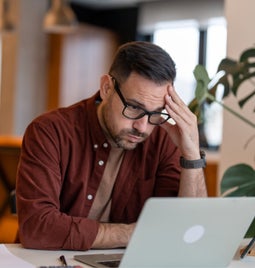 Man looking at his laptop screen with a frustrated look on his face and hand to his head