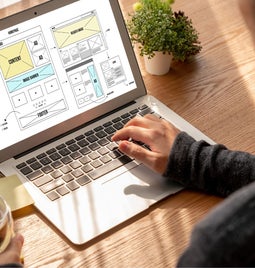 A man using his laptop with a homepage wireframe on the screen