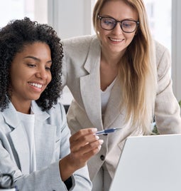 Two women smiling and pointing at a laptop screen