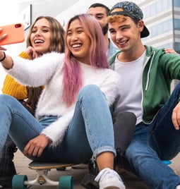 4 kids taking a selfie while sat on a skateboard in a parking lot