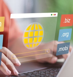 A person typing on a laptop surrounded by floating top level domains like .com, .edu, and .org, symbolizing web browsing.