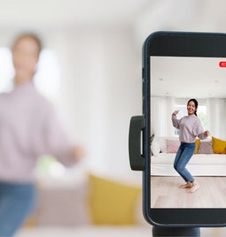 Photo of a woman behind a smartphone camera performing a TikTok dance trend