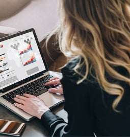 A woman typing on a laptop with graph data on the screen