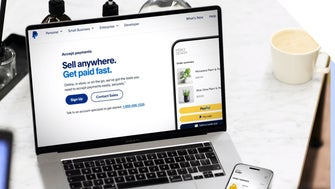 Laptop displaying PayPal's online payment options with a smartphone processing a transaction on the side.