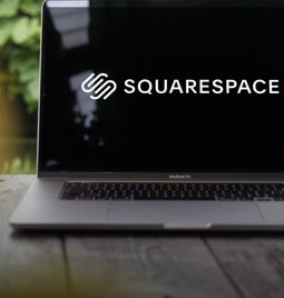 Laptop on a garden table with greenery in the background showing the Squarespace logo on the screen