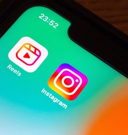 Close-up of a smartphone screen displaying the Instagram and Reels app icons against a gradient background