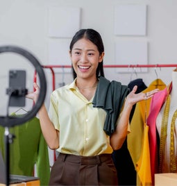 A woman in her clothes warehouse interacting with a camera in front of a ring light