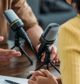 two people sat at wooden table facing each other speaking into microphones