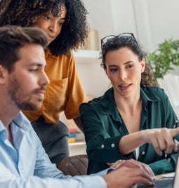Three people working around a laptop together