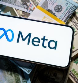 smartphone with meta logo on screen laying on top of a pile of cash