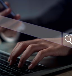 Person typing at a laptop keyboard with a transparent search bar powered by AI hovering above the hands