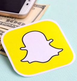 Sticker of snapchat logo laying on top of pile of dollar notes