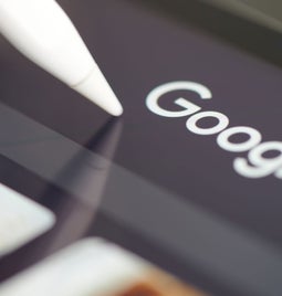 Closeup of a tablet screen with the Google logo and a stylus tapping it
