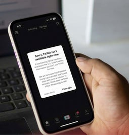 A hand holding a smartphone with a message from TikTok on the screen about the ban