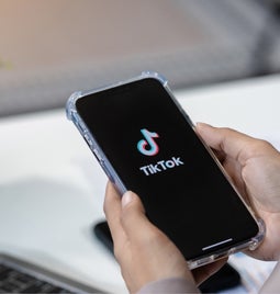 Hands holding a mobile showing the TikTok logo on the screen