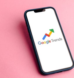 smartphone with the Google Trends logo on screen laying on a pink surface