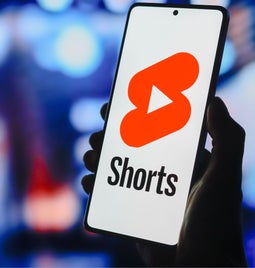 Photo of a hand holding a phone with the YouTube Shorts logo on screen